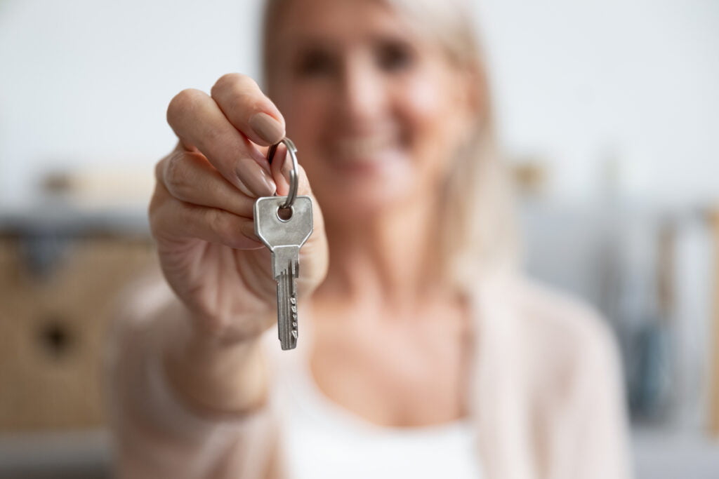 Senior Woman Holding Out House Key_Ways to Pay for Assisted Living